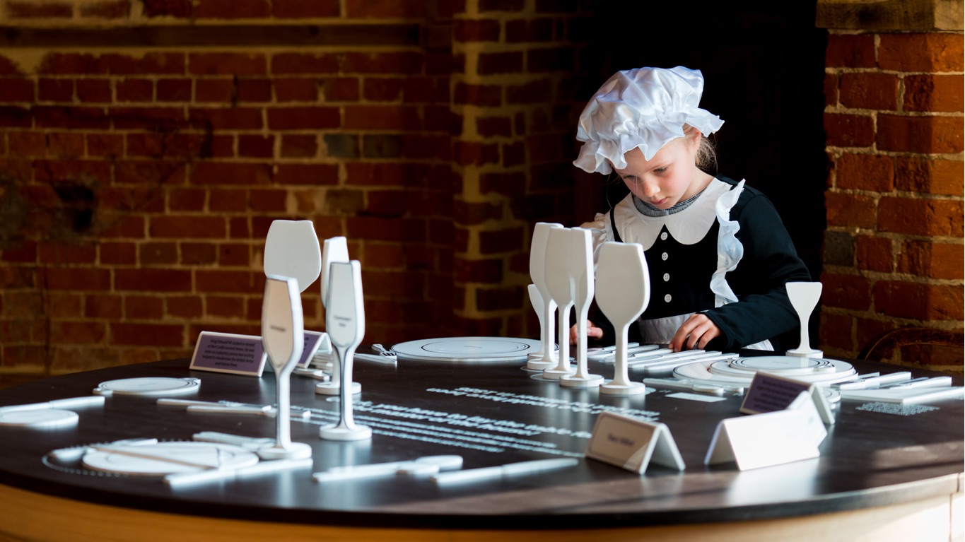 small girl dressed as victorian maid, completing puzzle of place settings on a table in Castle Dining Room
