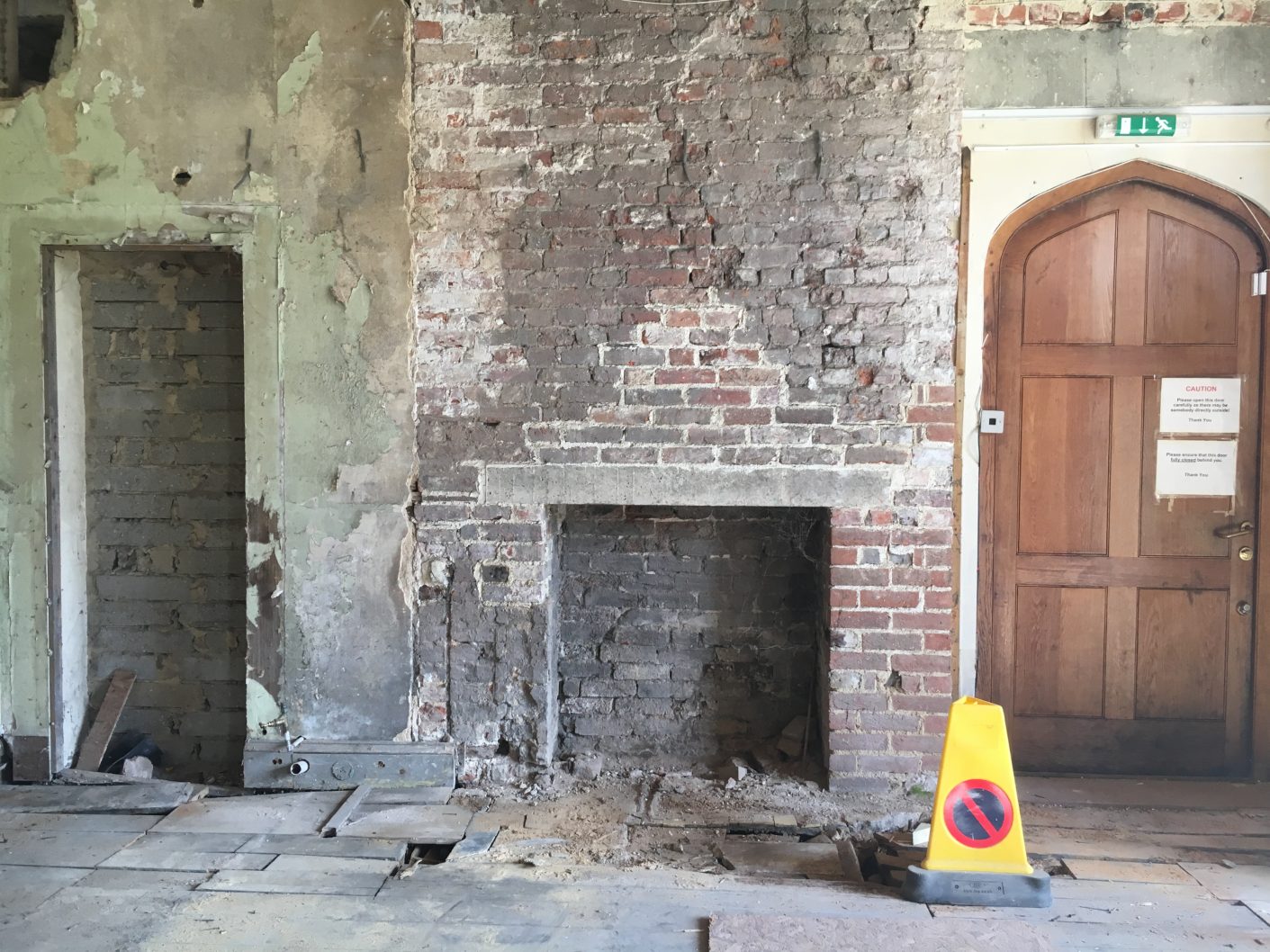 Open fireplace in brick wall with doorway to the left surrounded by bright green paintwork.