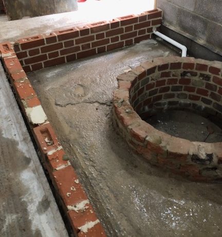 Brick well surrounded by newly laid concrete encased by low rectangular brick wall